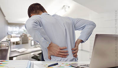 Person sitter vid skrivbord med ont i ryggen