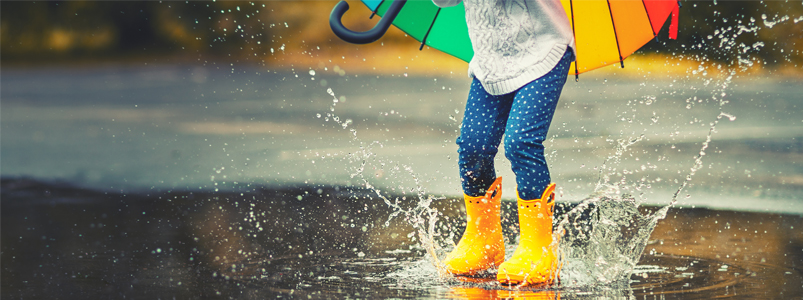 barn med gummistövlar som hoppar i en regnpöl