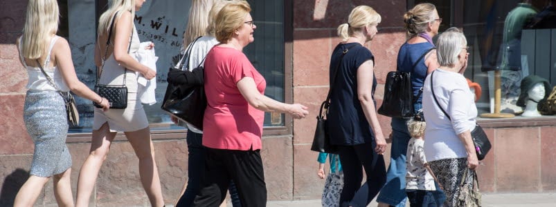 Sju kvinnor och två barn som promenerar på en gata i sommartid
