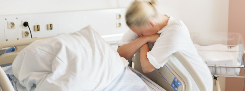 Kvinna under förlossning lutar sig mot sjuhussäng
