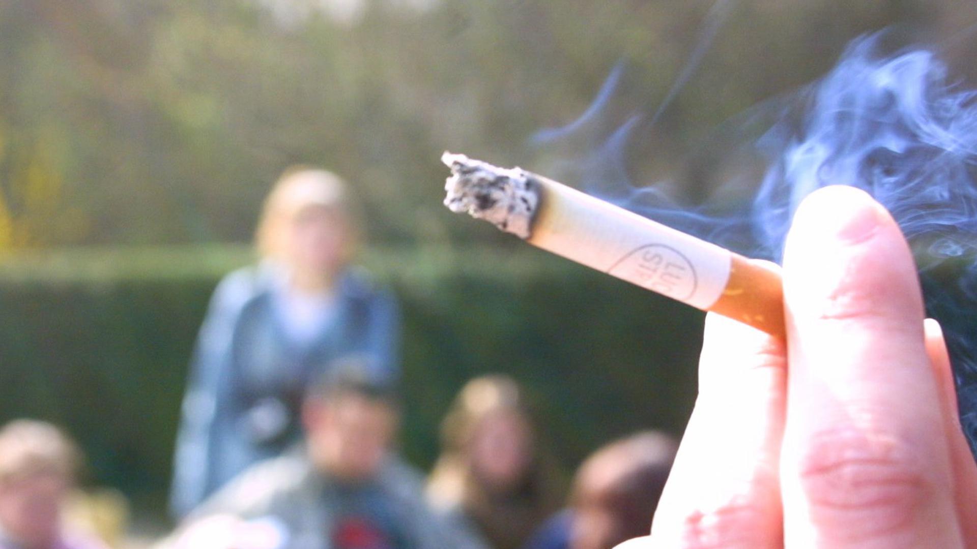 Cigarett hållen mellan två fingrar med ungdomar i bakgrunden