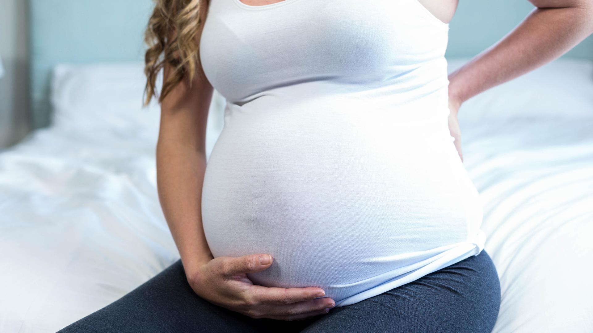 Gravid kvinna med tar sig för magen och ryggslut.