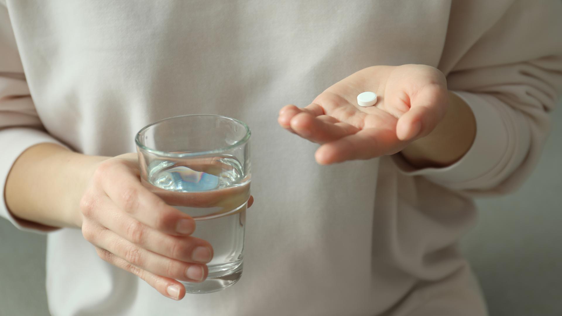 Kvinna som håller ett abortpiller i vänster hand och ett glas vatten i sin högra hand.