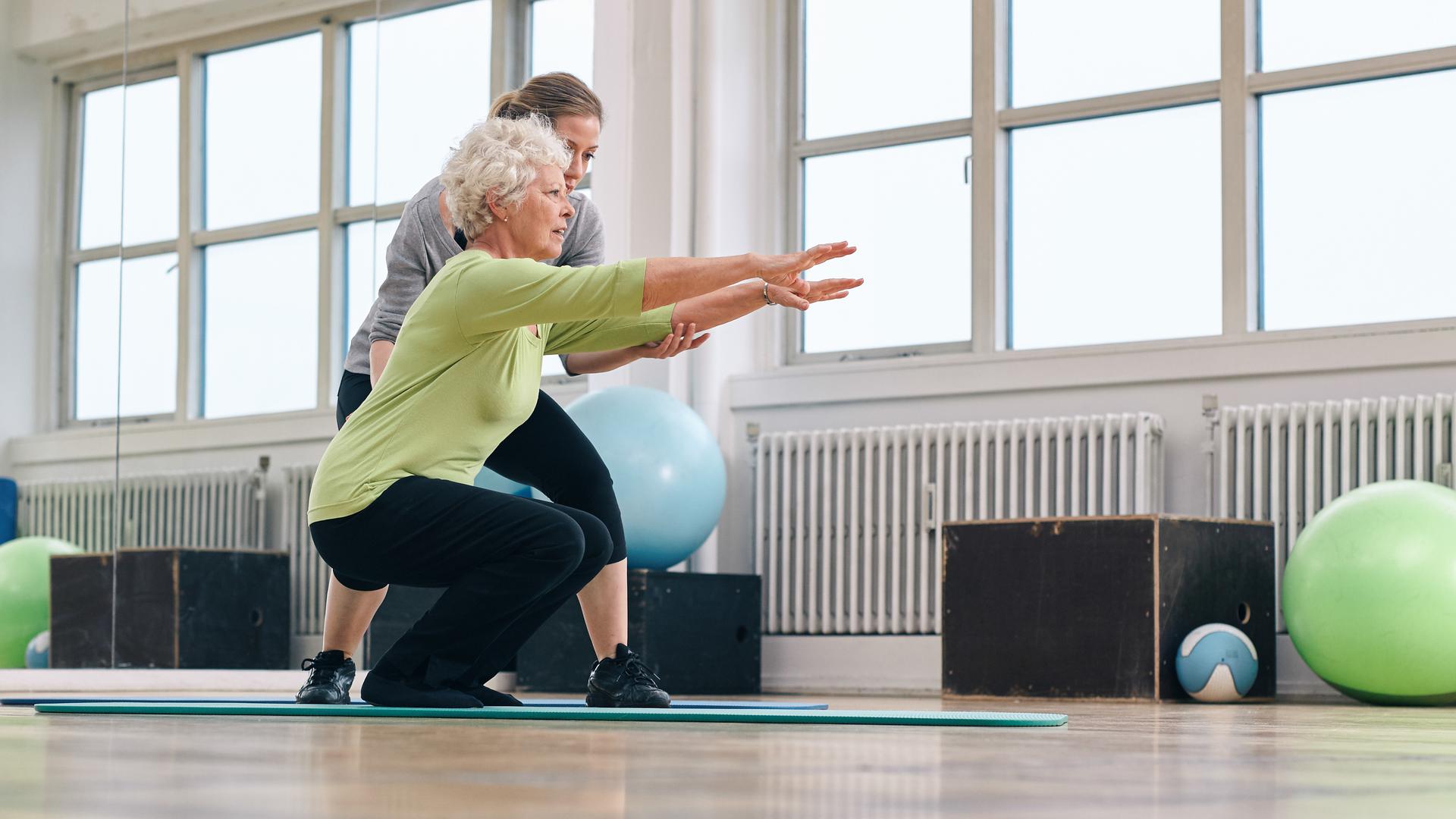 Senior kvinna gör motion med sin personliga tränare på gym. Gym instruktör hjälpa äldre kvinna i hennes träning.