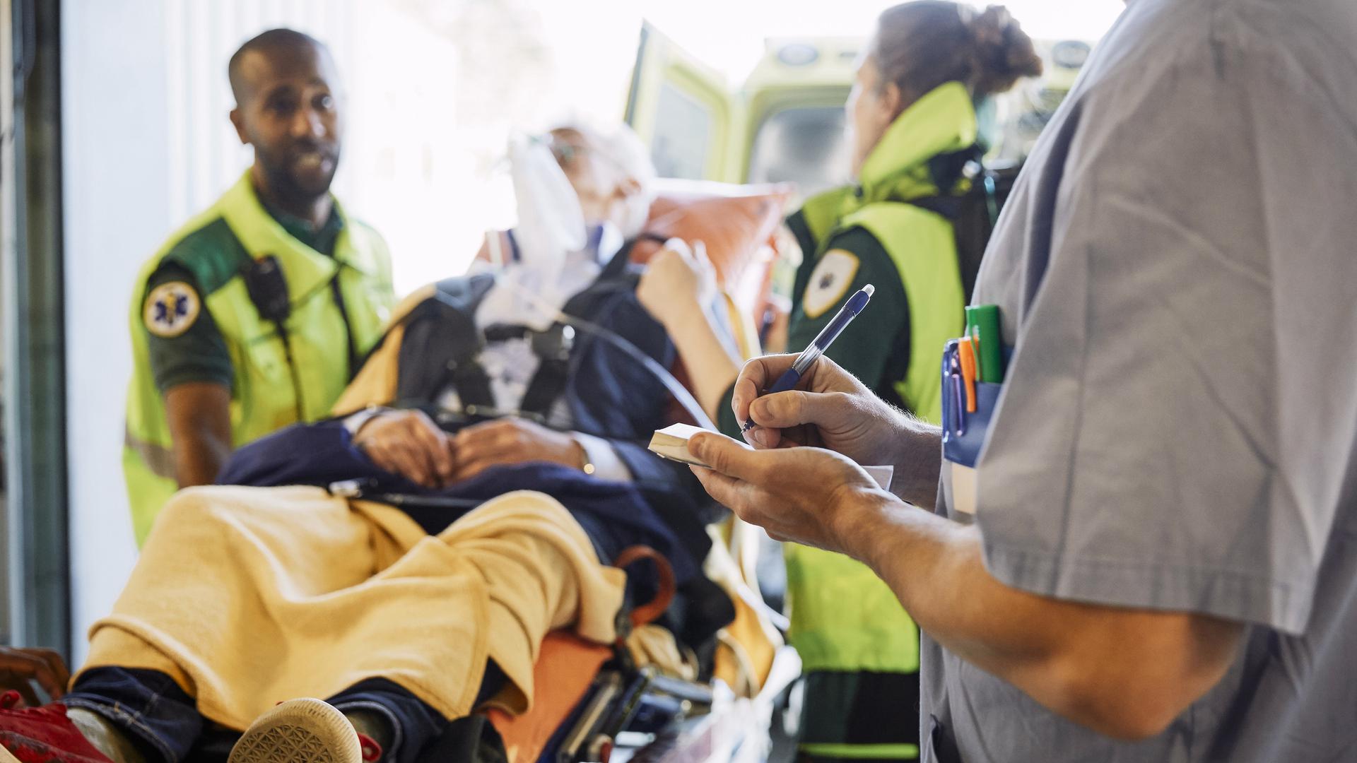 Midsection of male professional writing record against paramedics and patientÄldre man som kommer akut till sjukhus med ambulans