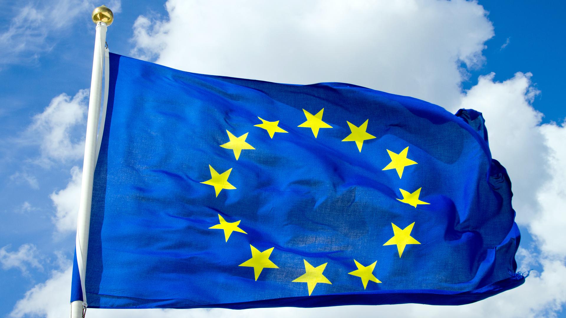 EU:s flagga som syns mot en molnig men solig himmel