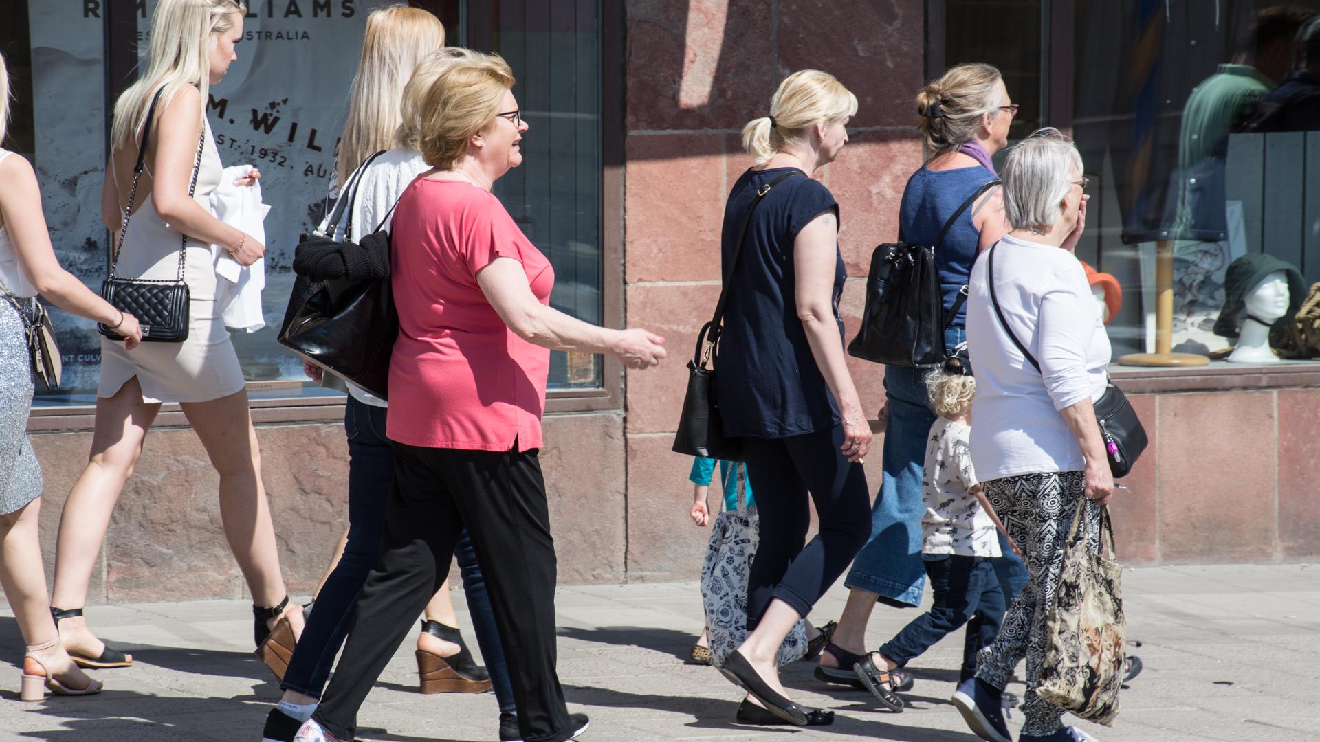 Sju kvinnor och två barn som promenerar på en gata i sommartid.