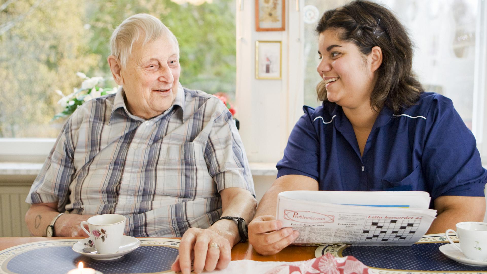 Äldre man får tidning uppläst av kvinna från hemtjänst