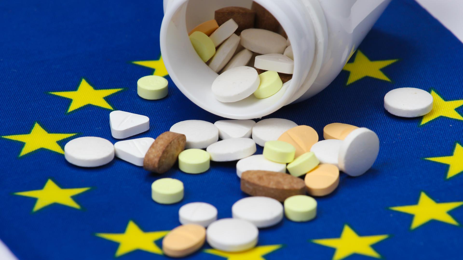 En medicinburk och olika tabletter som ligger på en EU-flagga.
