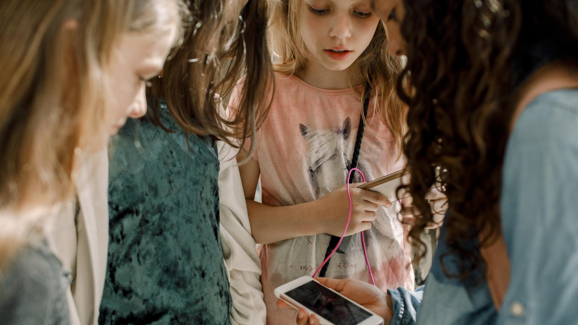 Fyra flickor i 10-årsåldern som tittar på en mobiltelefon.