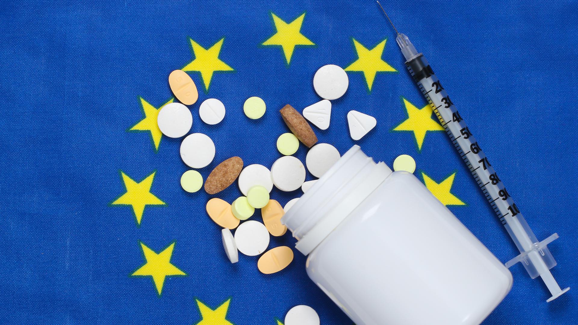 En medicinburk, olika tabletter och en spruta som ligger på en EU-flagga.