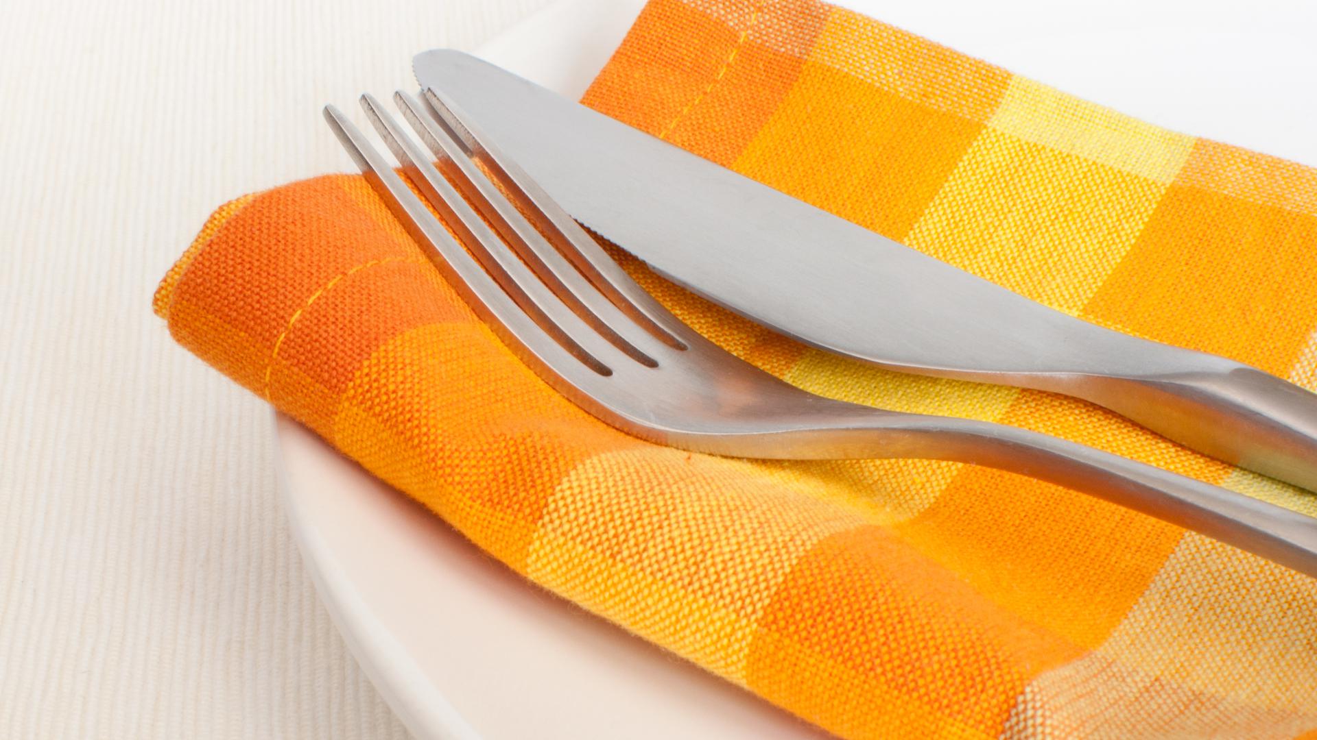 Bestick som ligger på en gul tygservett på en tallrik