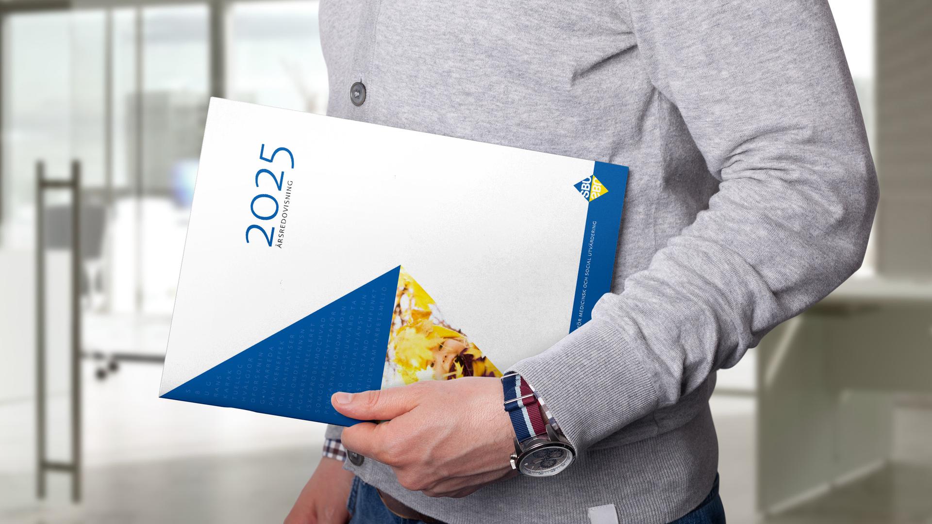 Man som håller SBU:s årsredovisning för 2025 i handen