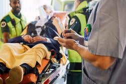 Midsection of male professional writing record against paramedics and patientÄldre man som kommer akut till sjukhus med ambulans