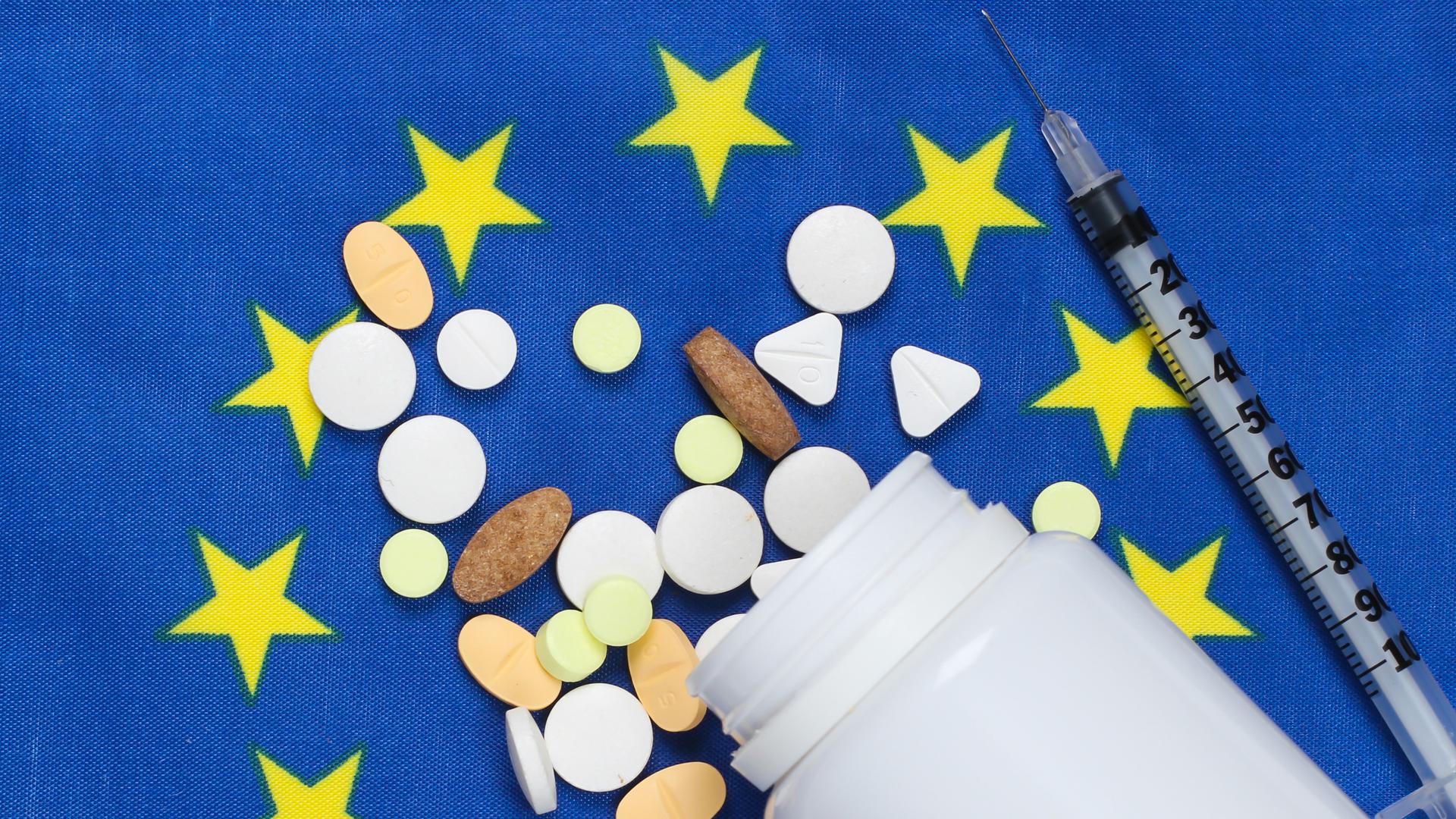 En medicinburk, olika tabletter och en spruta som ligger på en EU-flagga.