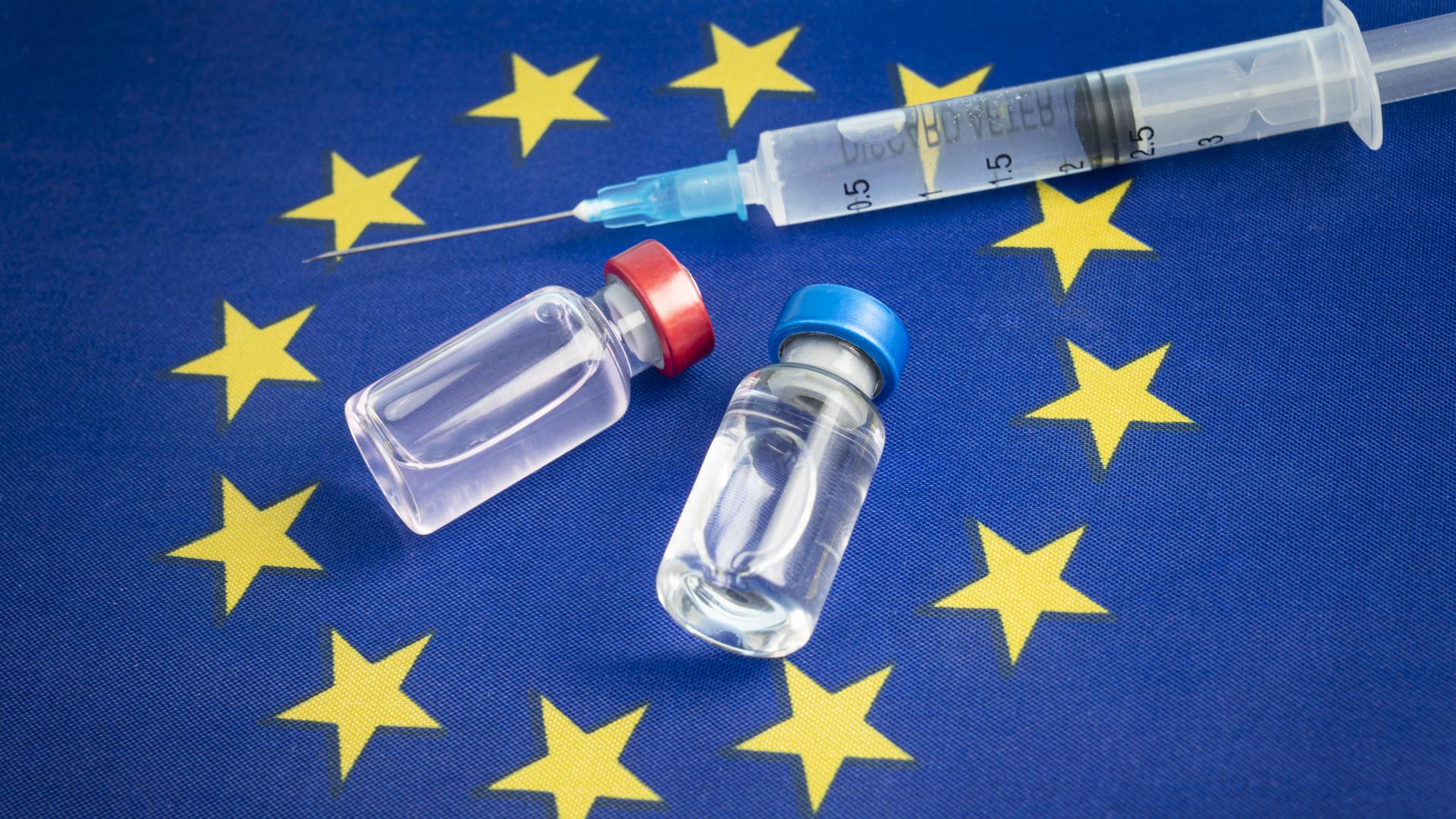 En spruta med en nål tillsammans med glasflaskor ligger på en EU-flagga.