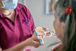 Tandl&auml;kare p&aring; tandl&auml;karmottagning som visar en patient hur man borstar t&auml;nderna eller tandprotes.