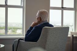Äldre man sitter ensam i en fåtölj och tittar ut genom fönstret