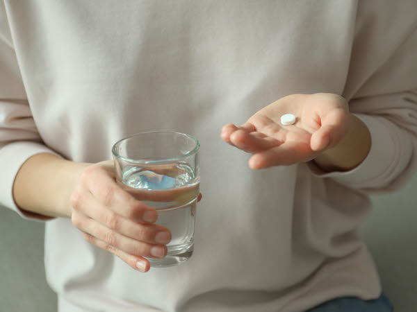 Kvinna som håller ett abortpiller i vänster hand och ett glas vatten i sin högra hand. 
