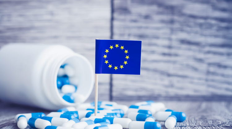 En medicinburk som vält och det ligger utspridda medicinkapslar på bordet. En EU-flagga står i mitten.