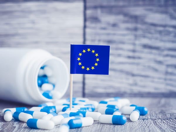 En medicinburk som vält och det ligger utspridda medicinkapslar på bordet. En EU-flagga står i mitten.