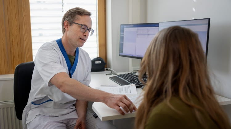 Sjukvårdspersonal i samtal med patient på sjukhus i mottagningsrum