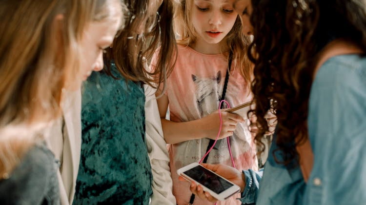 Fyra flickor i 10-årsåldern som tittar på en mobiltelefon.