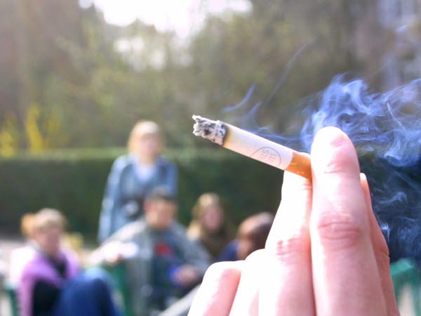 Cigarett hållen mellan två fingrar med ungdomar i bakgrunden