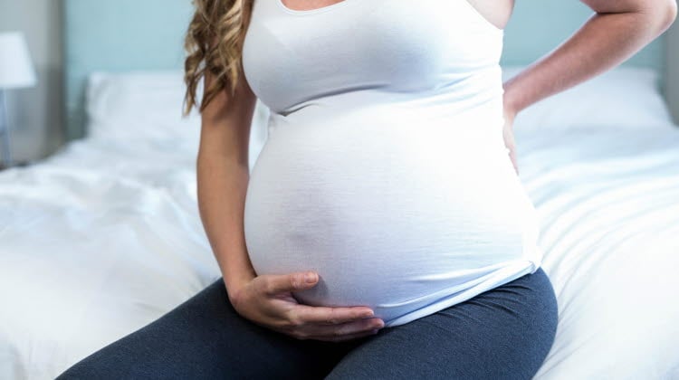 Gravid kvinna med tar sig för magen och ryggslut.