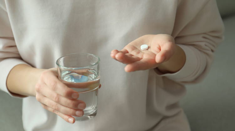 Kvinna som håller ett abortpiller i vänster hand och ett glas vatten i sin högra hand. 