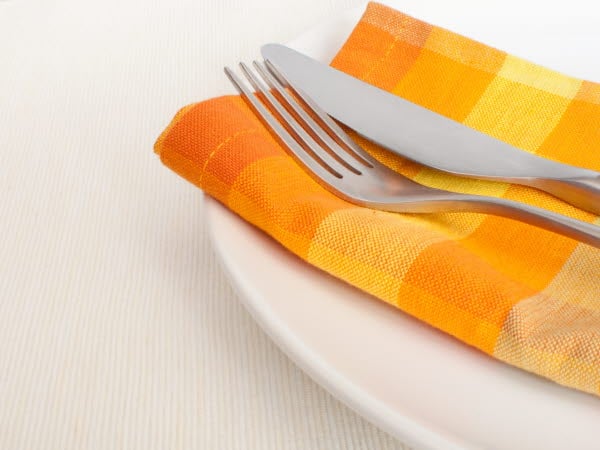Bestick som ligger på en gul tygservett på en tallrik