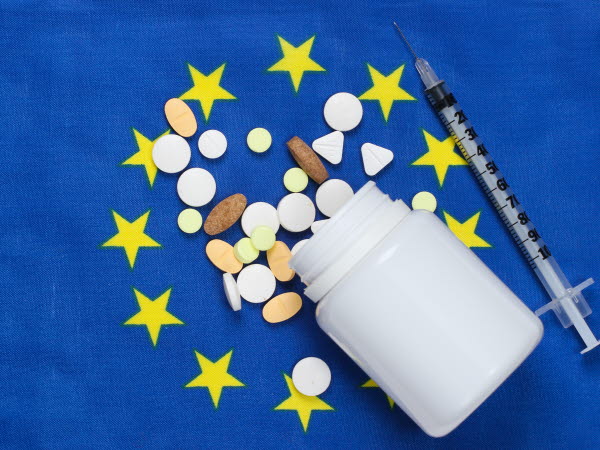 En medicinburk, olika tabletter och en spruta som ligger på en EU-flagga.