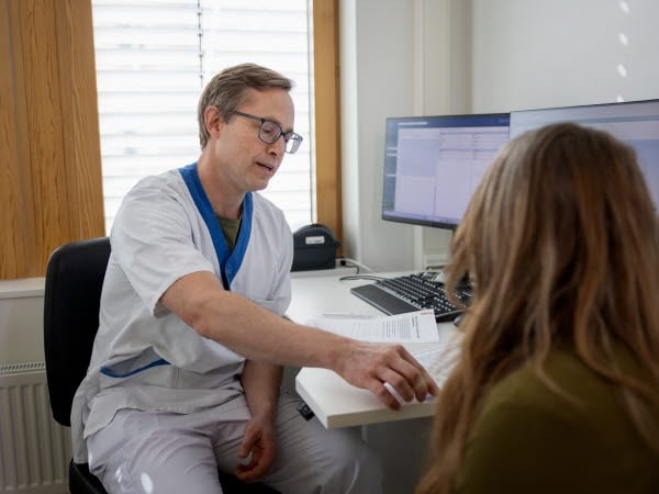 Sjukvårdspersonal i samtal med patient på sjukhus i mottagningsrum